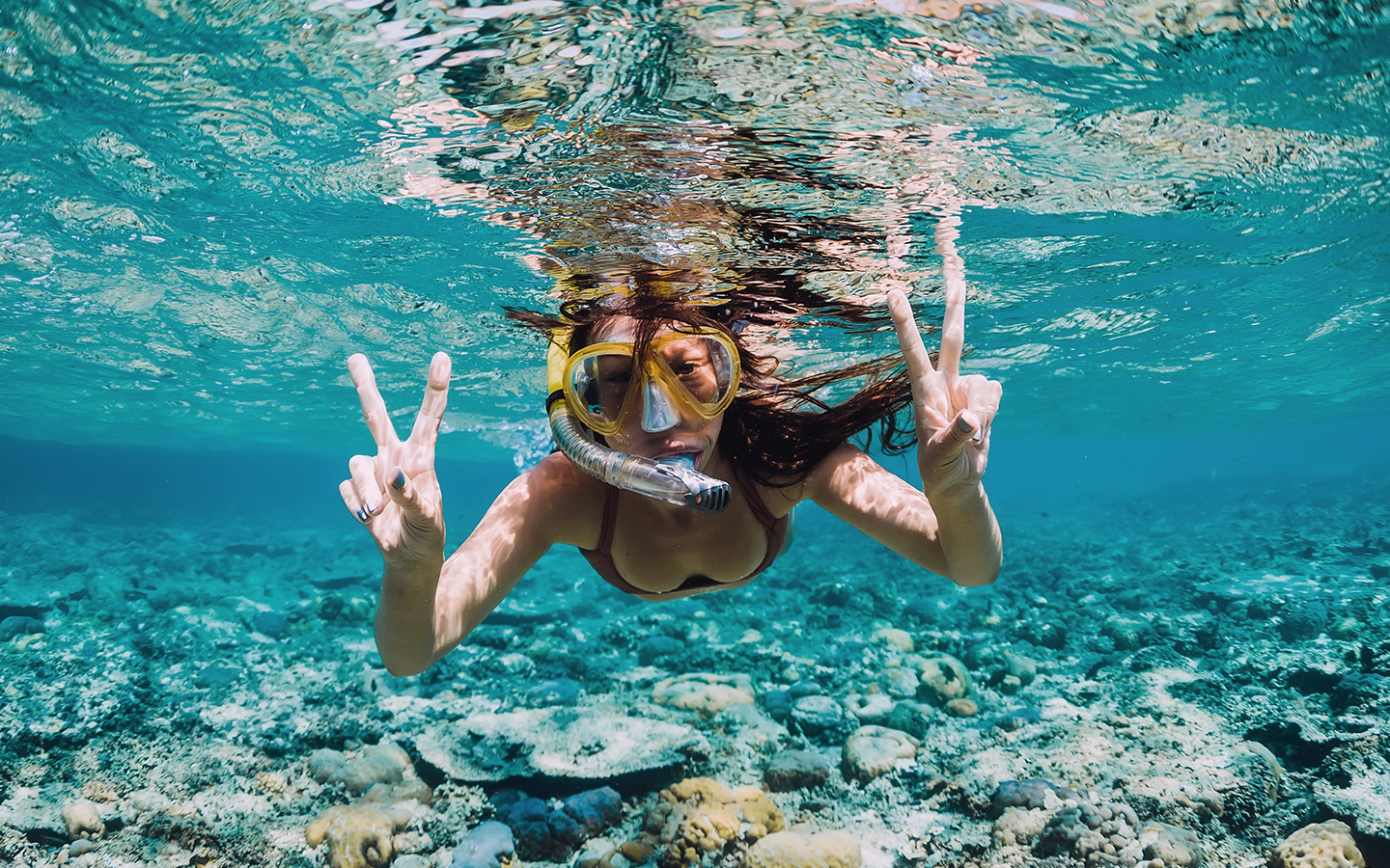 Woman snorkels while flashing peace sign underwater with both hands